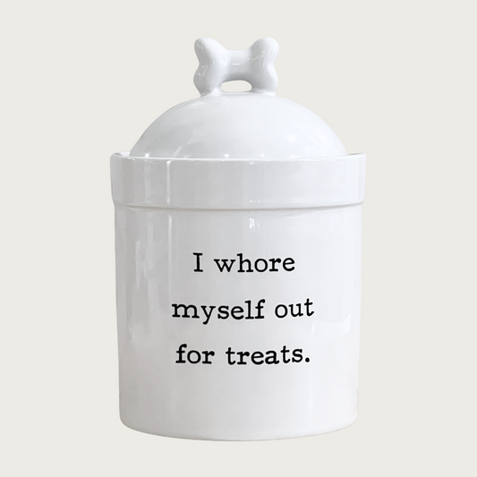 White ceramic dog treat jar with bone-topped lid. Sarcastic text in center reads "I whore myself out for treats." in black.