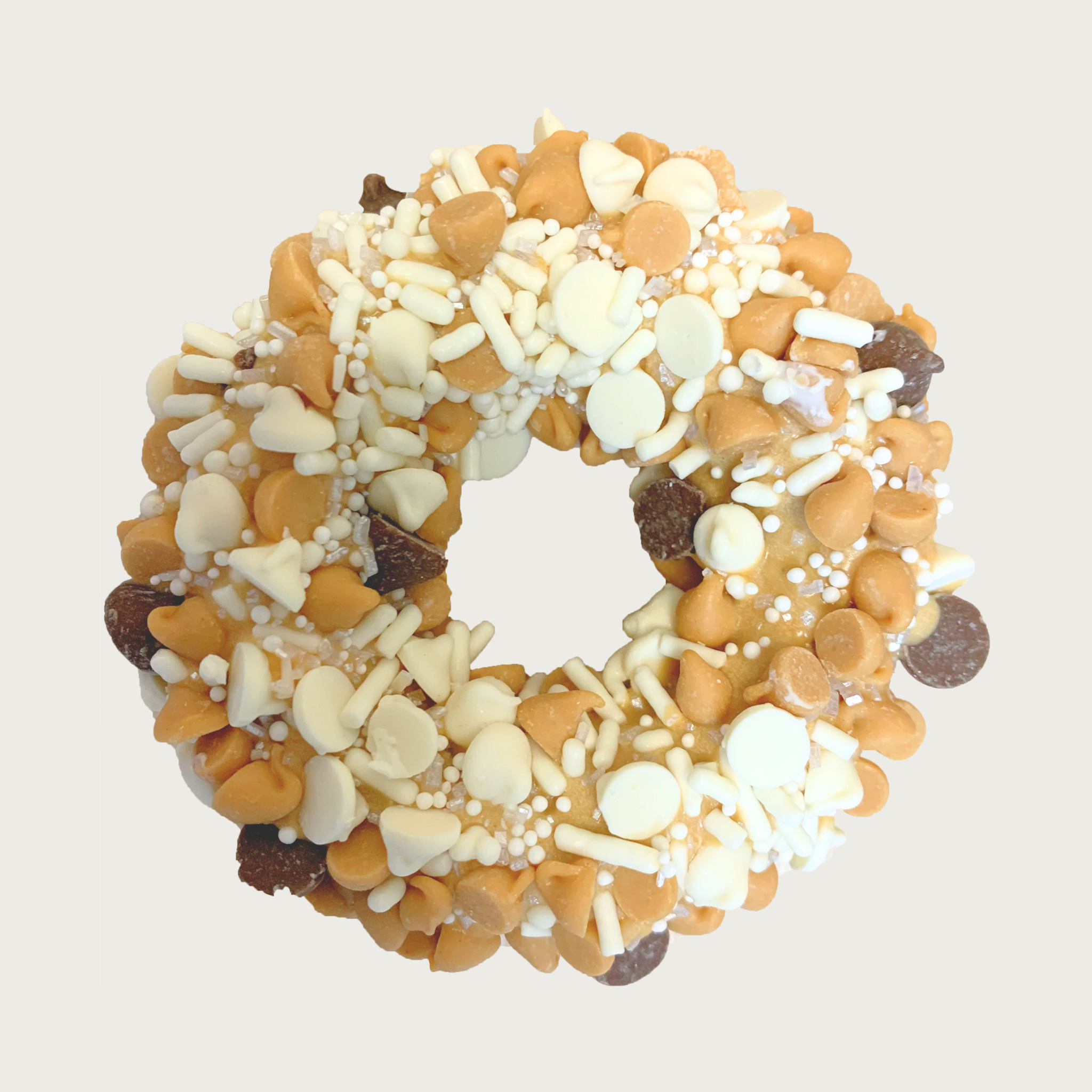 Thick, donut-shaped dog cookie decorated with mini peanut butter, vanilla, and carob drops, and white sprinkles.