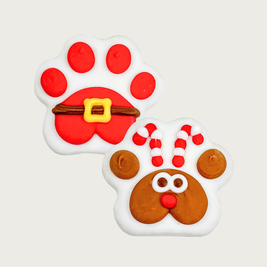 Two Christmas themed paw print shaped dog cookies. Both are covered in a white coating. One has red toes & red paw pad with Santa belt across it. The other has a brown paw pad decorated to look like Rudolph, with 2 brown toes for "ears" and accented with 2 candy cane antlers.