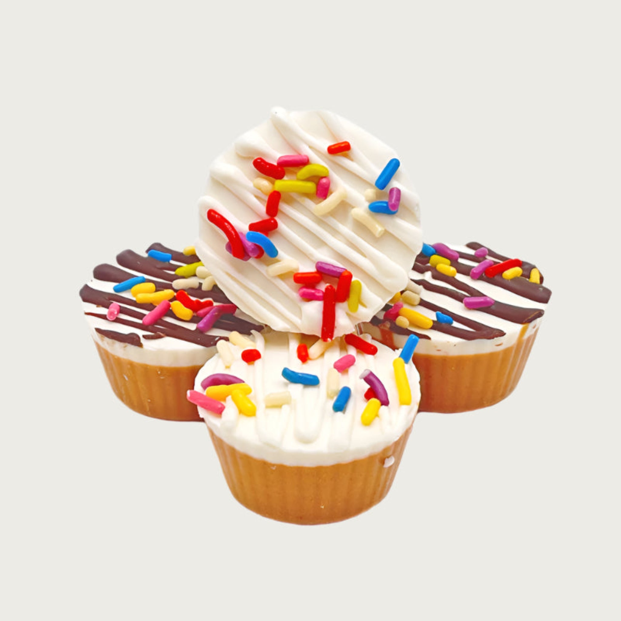 A stack of four peanut butter cup dog treats. Side view shows 3/4 of the cup is peanut butter with the top 1/4 a white coating. They are drizzled in white or brown, and topped with multicolored sprinkles.