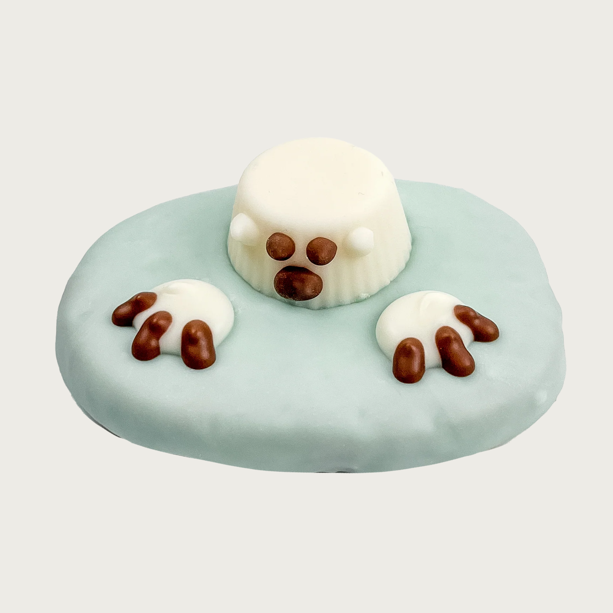 Round dog cookie covered in pale blue icing to look like water. Decorated to look like a polar bear coming out of the water, with white icing paws & brown claws, and an upside down white peanut butter cup with brown eyes and nose, and tiny white ears.