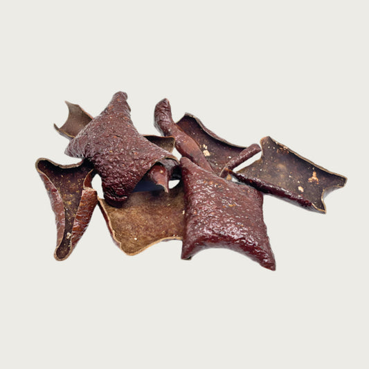 Close-up of a small pile of Wet Nose Pork Crispies treats. They are dark brown, thin squares about 2.5" wide, with a bumpy texture & curled edges.