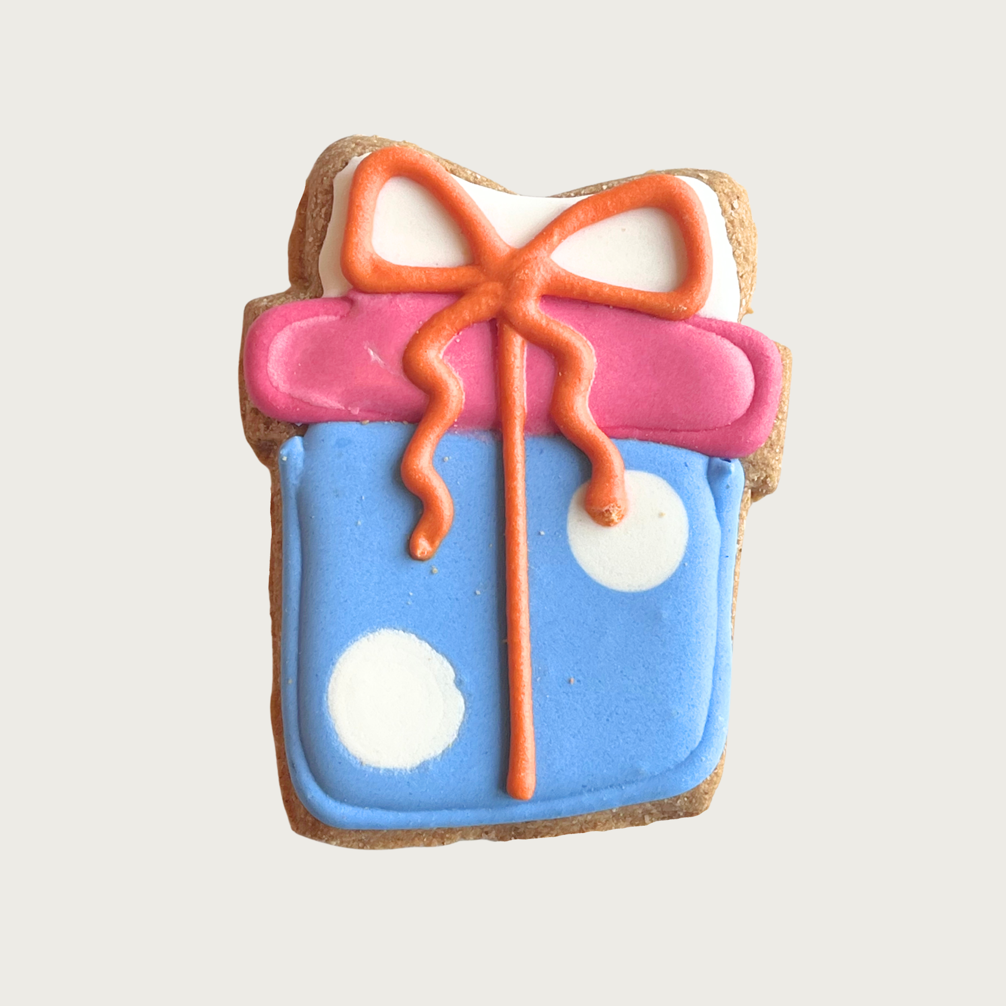 Decorative dog cookie shaped like a gift box. The box is iced in light blue with two white polka dots, its lid is pink, and the bow & ribbon are orange.