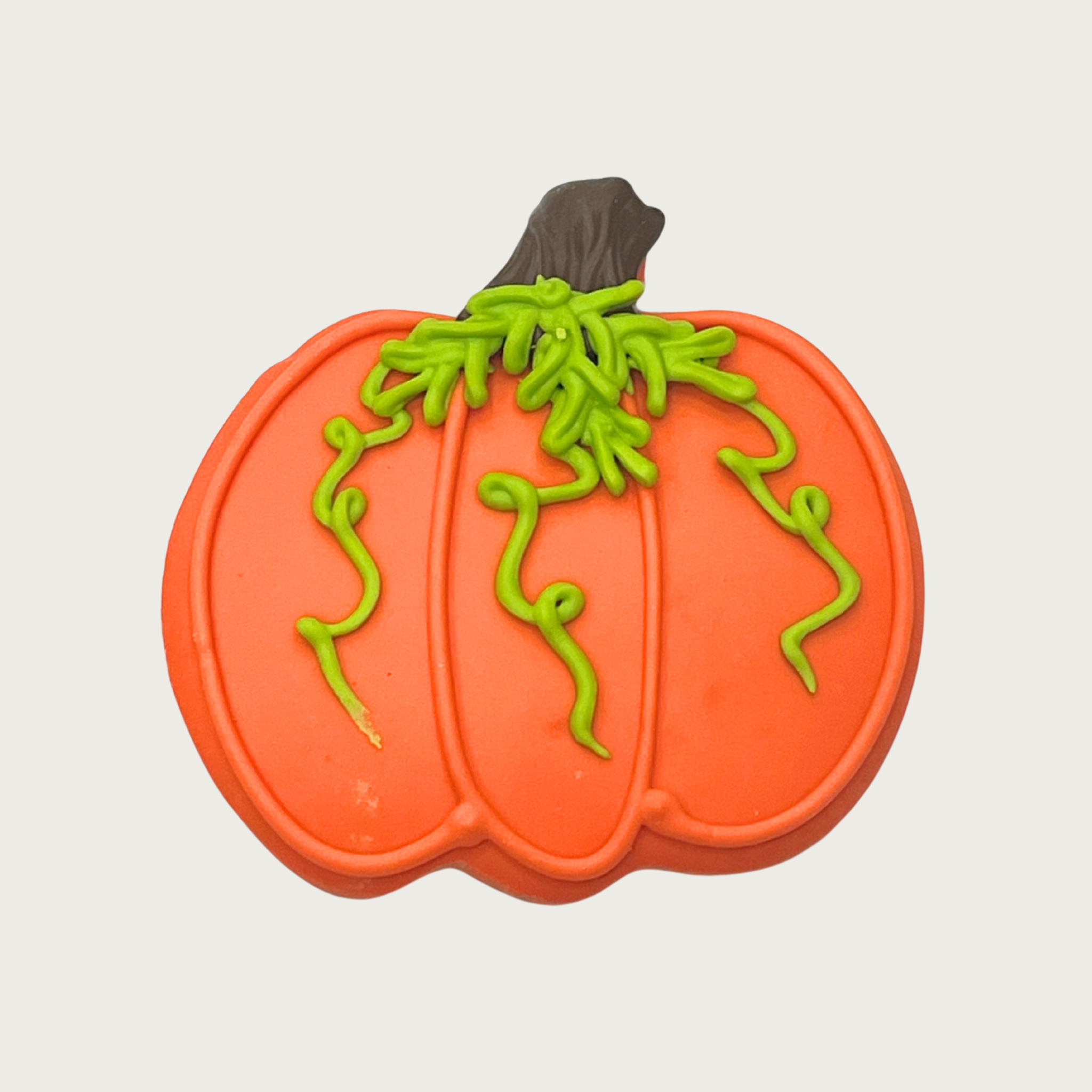 Decorated pumpkin-shaped dog cookie. Body is orange, with thick brown stem, and green vines trailing down the front of the pumpkin.