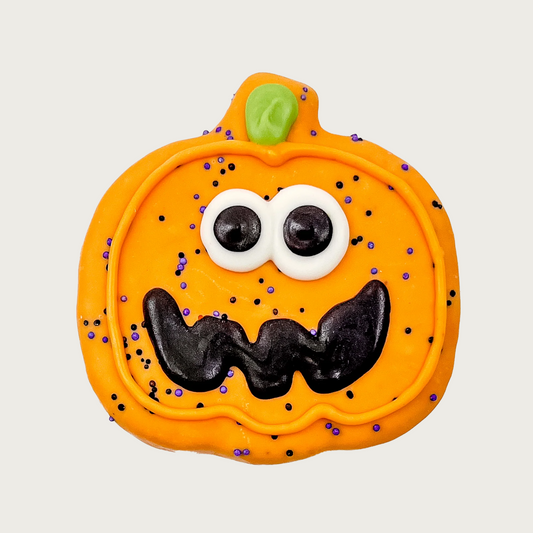 Dog cookie shaped like a Halloween jack o'lantern with googly eyes, black jagged smile, with tiny purple sprinkles.
