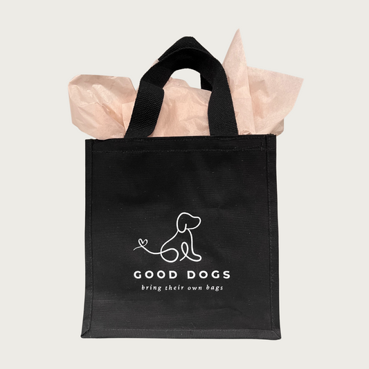 Black tote bag with white line illustration of a dog in center. Beneath it reads "GOOD DOGS bring their own bags" in white text.
