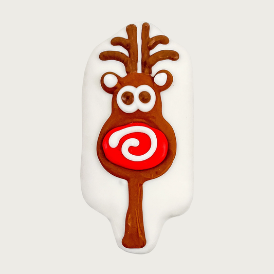 White, oblong shaped dog cookie with reindeer decoration. Brown reindeer from antlers to a long, skinny neck, focused on its face, with big eyes, and even bigger red nose with a white swirl.