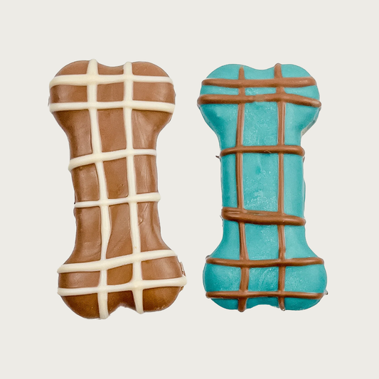 Two dog cookie shaped like dog bones, one brown with white crosshatch pattern and the other teal blue with brown crosshatch pattern.