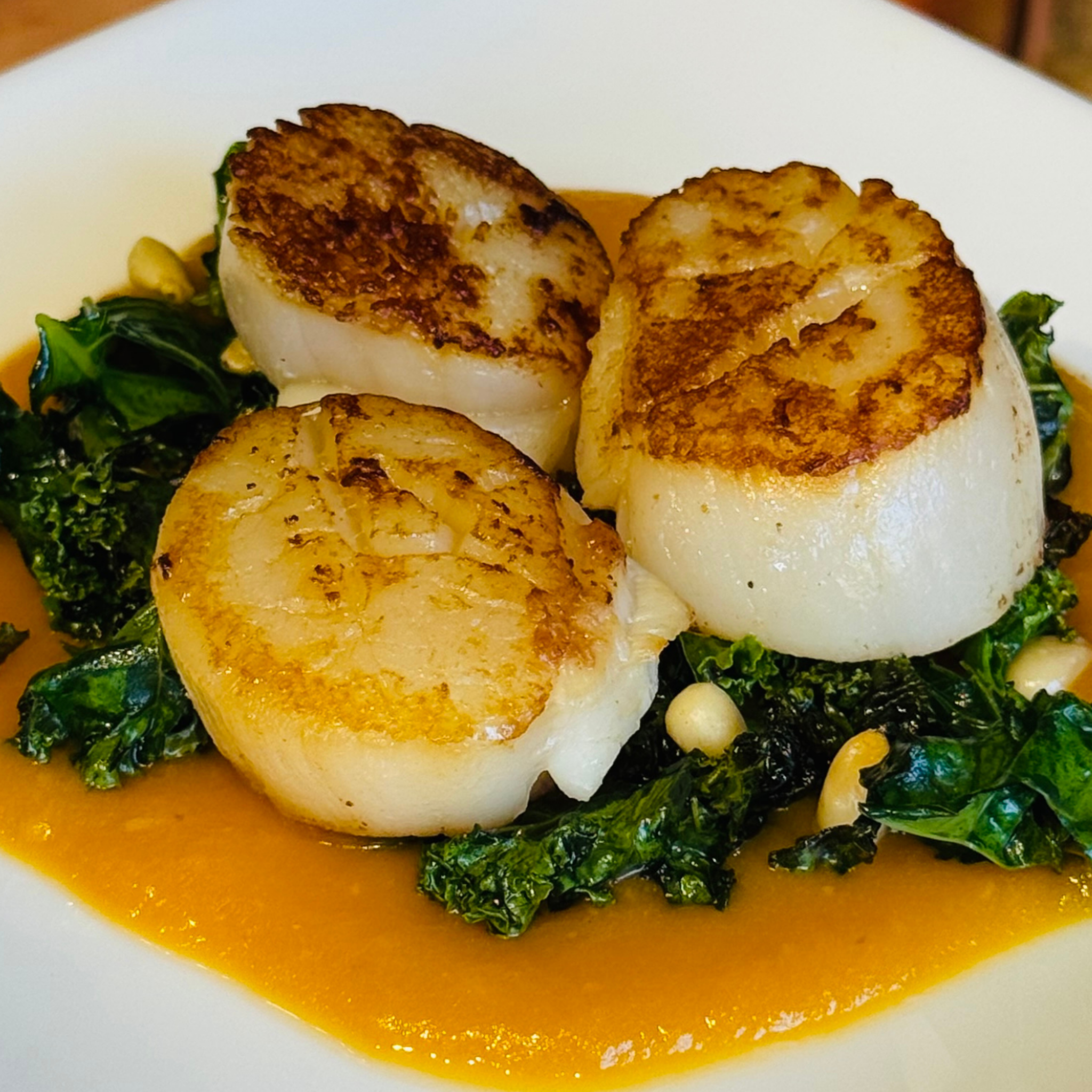 Three pan seared scallops on a bed of greens, on top of a creamy orange sweet potato puree.