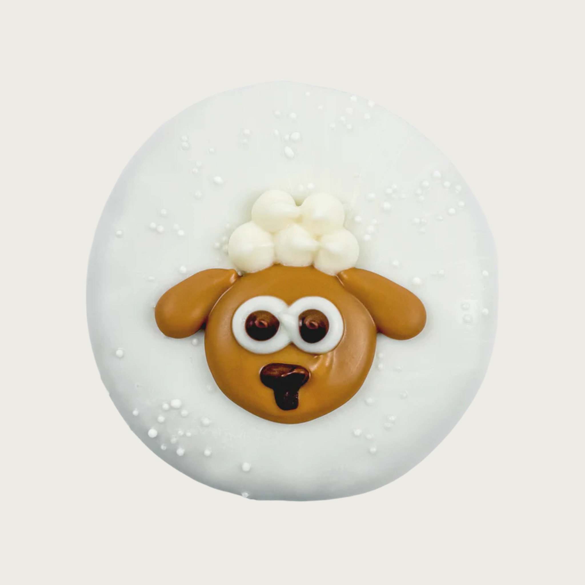 Round dog cookie covered in white frosting, with iced image of a brown lamb with poufy white fur on its head in its center.