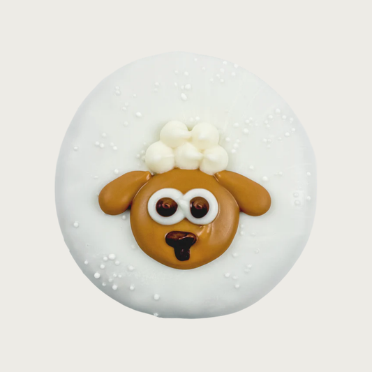 Round dog cookie covered in white frosting, with iced image of a brown lamb with poufy white fur on its head in its center.