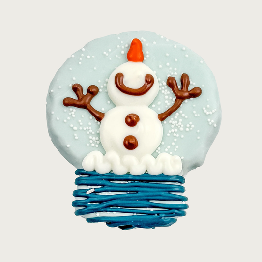 Dog cookie decorated to look like a snowglobe. Top globe section is covered in pale blue icing to look like the sky, with white nonpareils to look like falling snow. In the center is a snowman looking up, with his orange carrot nose pointing up, and a big brown smile, with brown stick arms and brown buttons down his belly. Base has darker blue drizzle.