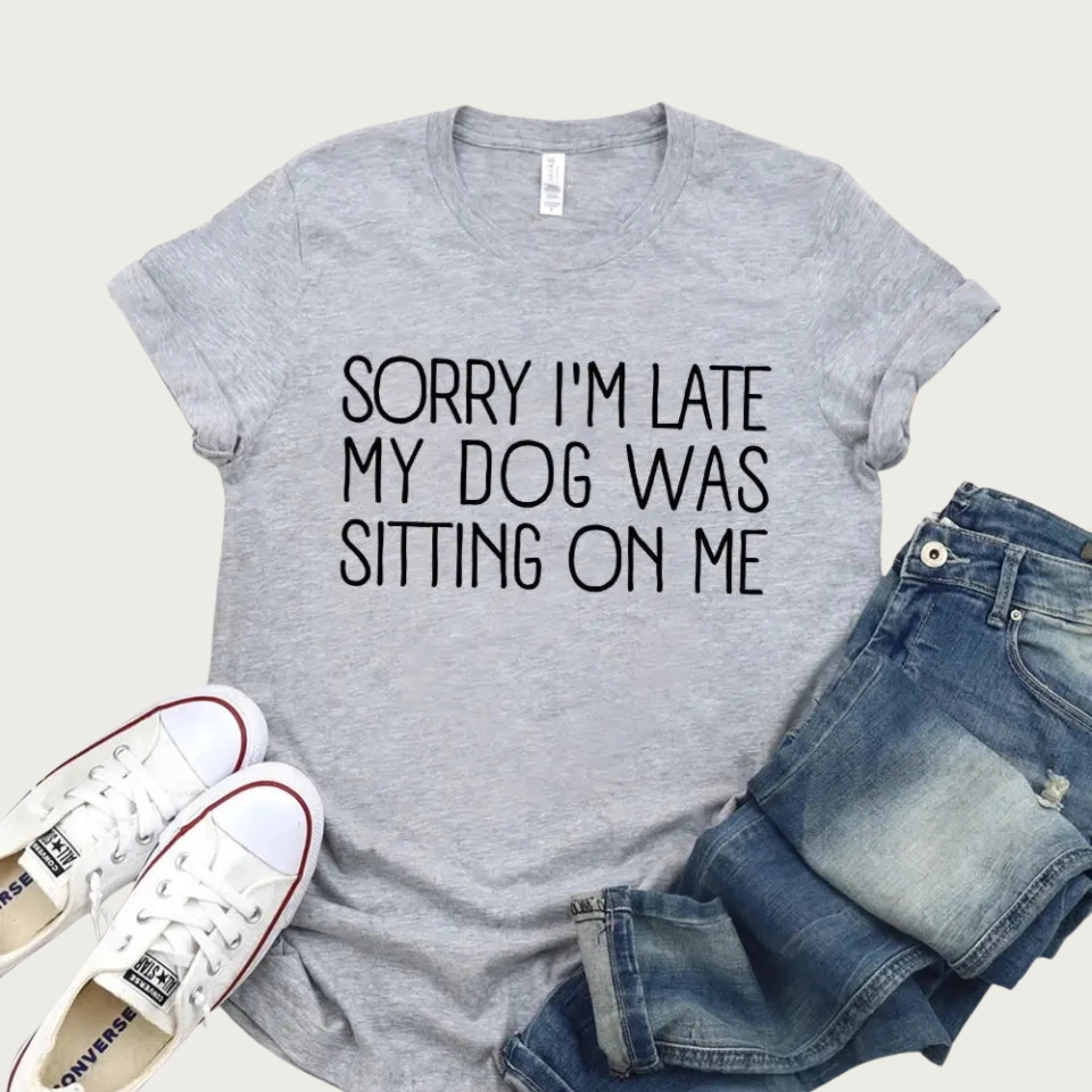 Medium gray heathered t-shirt with 'Sorry I'm late my dog was sitting on me' in thin black all caps text, staged with white sneakers and jeans.
