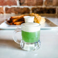 Load image into Gallery viewer, Alternate image of the St. Patrick's Fish & Chips dinner, with the "green beer" in plastic mug as the focal point. The plated dinner is in the background.
