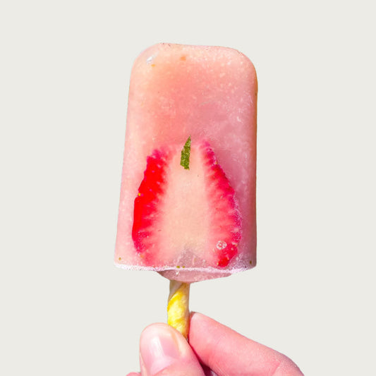 Pink popsicle with a large strawberry slice inside.