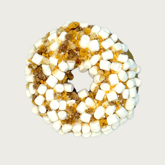 A thick donut shaped dog cookie,  topped with white mini marshmallows and golden-brown sugar crystals.