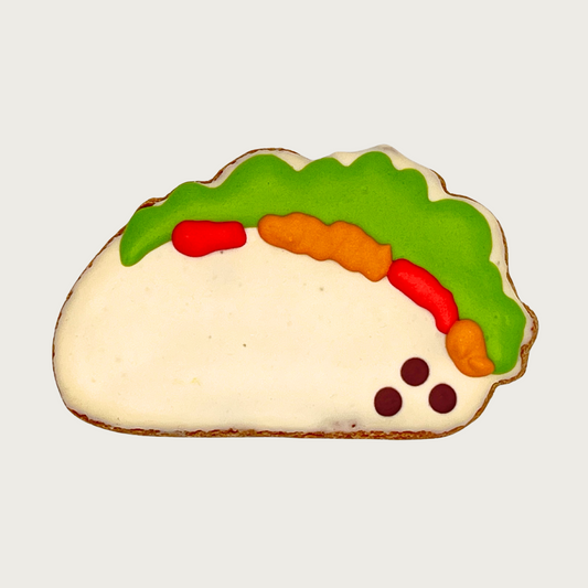 Dog cookie shaped like a taco with green, red, and orange toppings in a light beige shell.