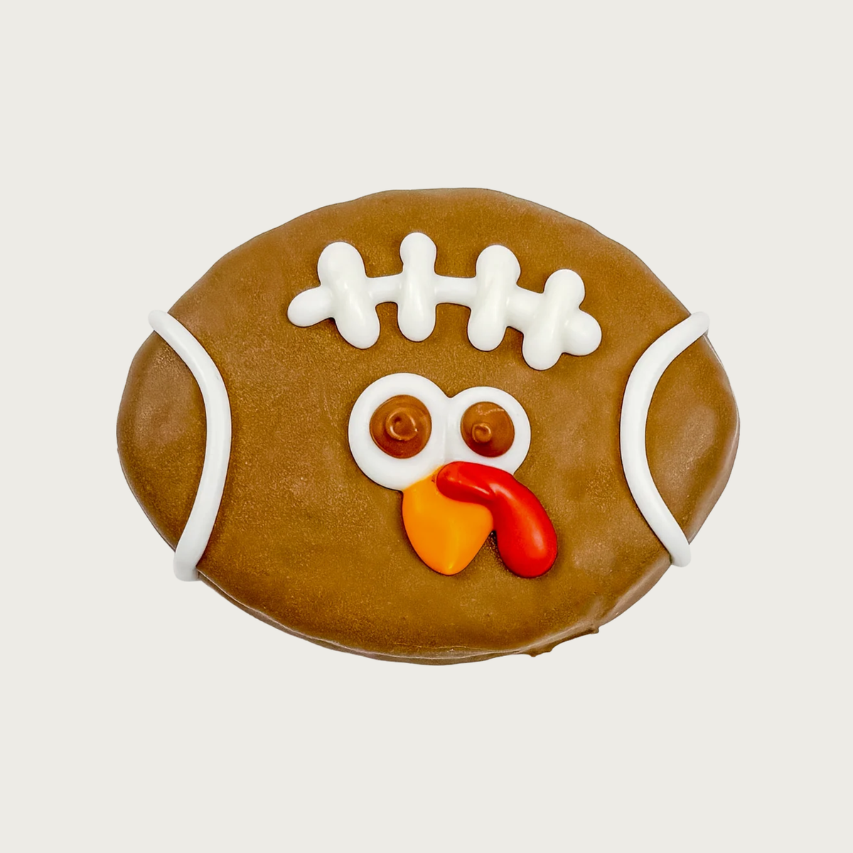 A football-shaped dog cookie decorated with brown icing, white icing laces, and a turkey face with white & brown eyes, orange beak, and red wattle.