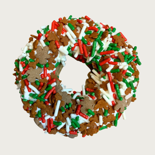 Christmas themed, donut shaped dog cookie decorated with tiny brown gingerbread men and red, white & green sprinkles. 