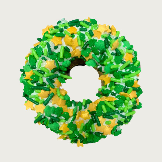 St. Patrick's Day themed, donut shaped dog cookie dipped in yogurt coating, and covered with clover decorettes, gold stars, and sprinkles in varying shades of green.