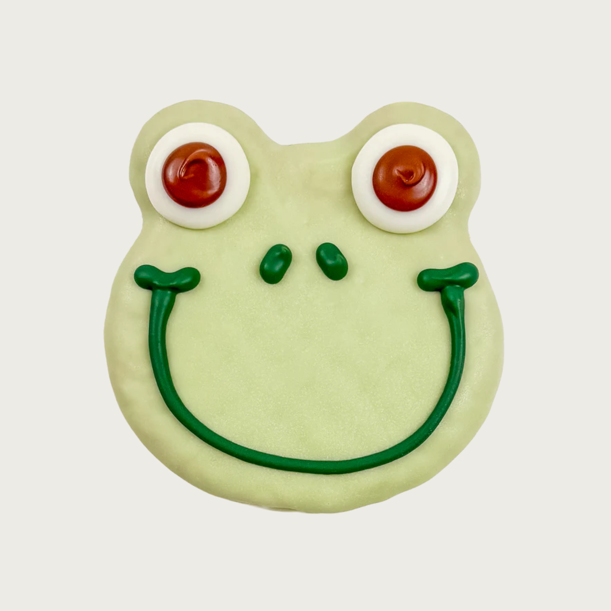 Dog cookie shaped like a frog's face. It is pale green with big eyes, and a simple smile piped in green icing.