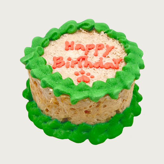 Small round dog/cat cake with green frosting on the edges, with 'Happy Birthday' written on top with a pawprint.