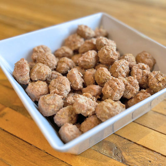 A square white bowl filled with homemade turkey, bacon, and apple meatballs for pets, on a wooden table.
