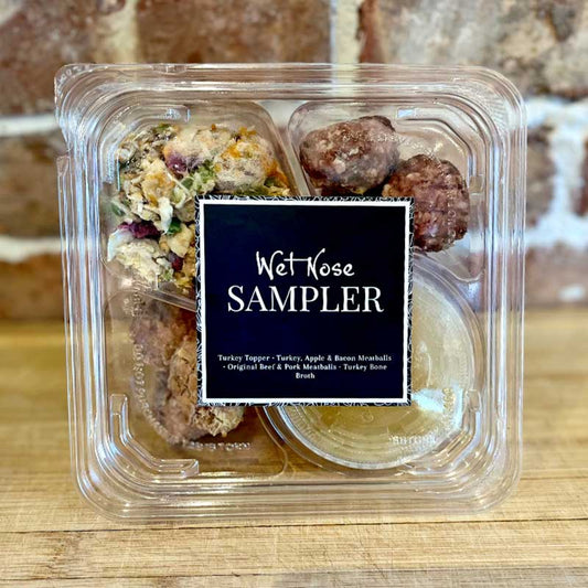 A plastic, sectioned to-go container labeled 'Wet Nose SAMPLER' with an assortment of fresh food for pets, including turkey topper, turkey bone broth, turkey, bacon & apple meatballs, and original meatballs.