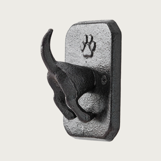 Dark metal, rectangular decorative wall hook that features a 3D dog rear end sticking out with its tail standing up. A paw print detail is on the flat part of the hook and is above the dog body.