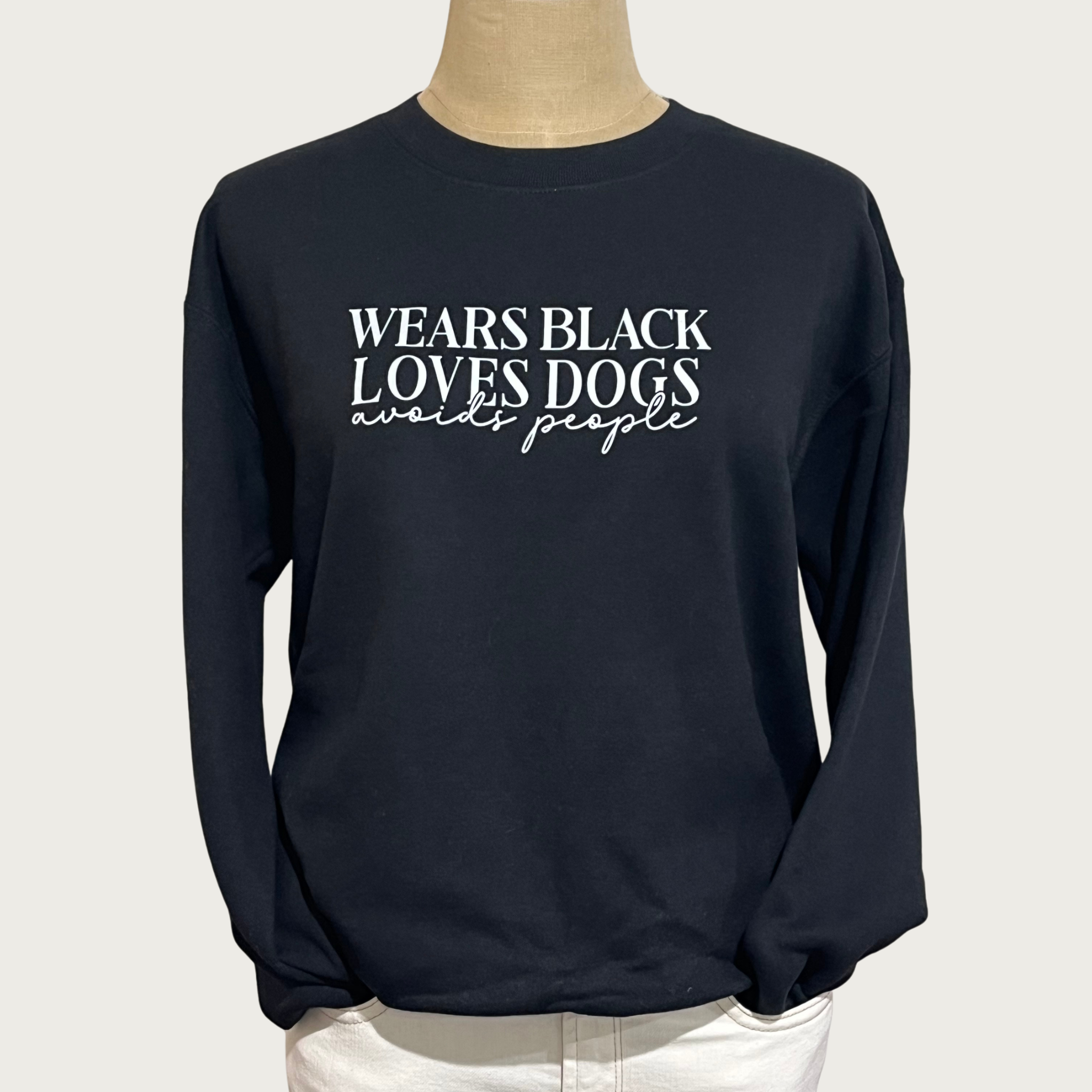 A black long-sleeve crewneck sweatshirt displayed on a mannequin torso. The sweatshirt features the text 'WEARS BLACK LOVES DOGS avoids people' printed in white across the chest. 'WEARS BLACK LOVES DOGS' is in all caps, serif font. 'avoids people' is in lower case script font.