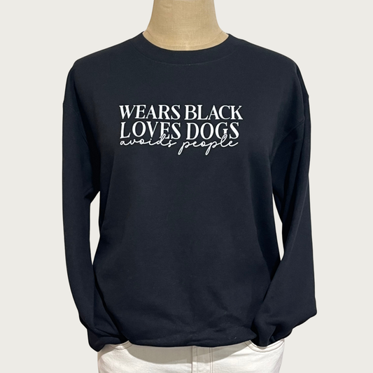A black long-sleeve crewneck sweatshirt displayed on a mannequin torso. The sweatshirt features the text 'WEARS BLACK LOVES DOGS avoids people' printed in white across the chest. 'WEARS BLACK LOVES DOGS' is in all caps, serif font. 'avoids people' is in lower case script font.