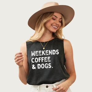 Blonde model wearing a tan hat, wearing this tank top. It has a crew neck, is sleeveless, and features "Weekends Coffee & Dogs" in washed white text. Top color is a washed looking shade of black - almost dark charcoal gray.