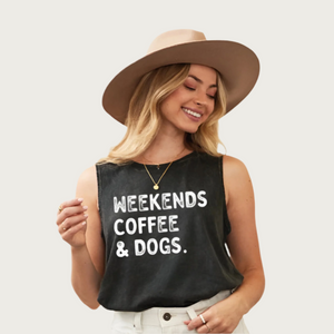 Blonde model wearing a tan hat, wearing this tank top. It has a crew neck, is sleeveless, and features "Weekends Coffee & Dogs" in washed white text. Top color is a washed looking shade of black - almost dark charcoal gray.