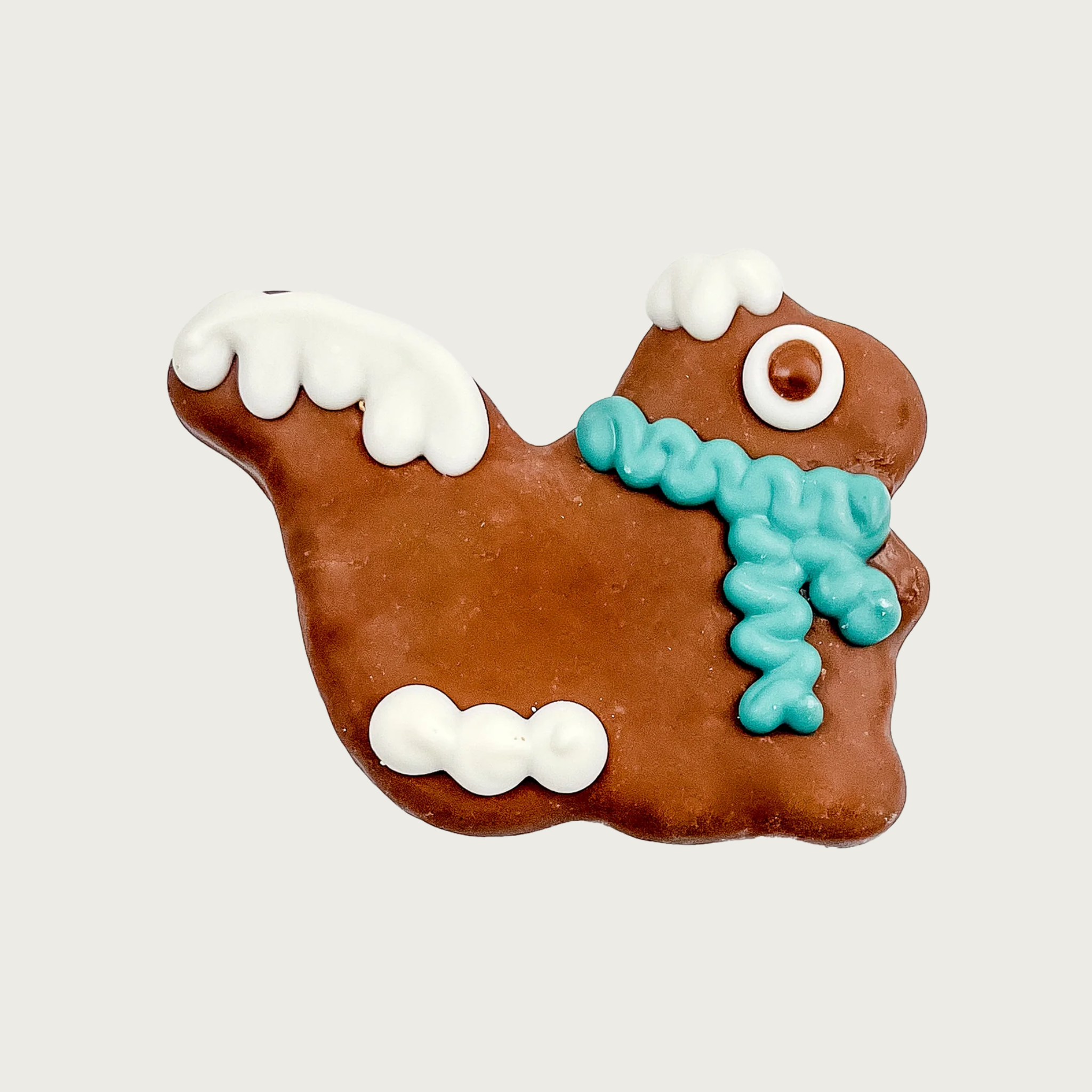 Decorated dog cookie shaped like the side view of a squirrel with a bushy tail. Its body is dark brown with white icing "snow" on top of its head, tail and feet. It has a light teal blue scarf, and a big googly eye.