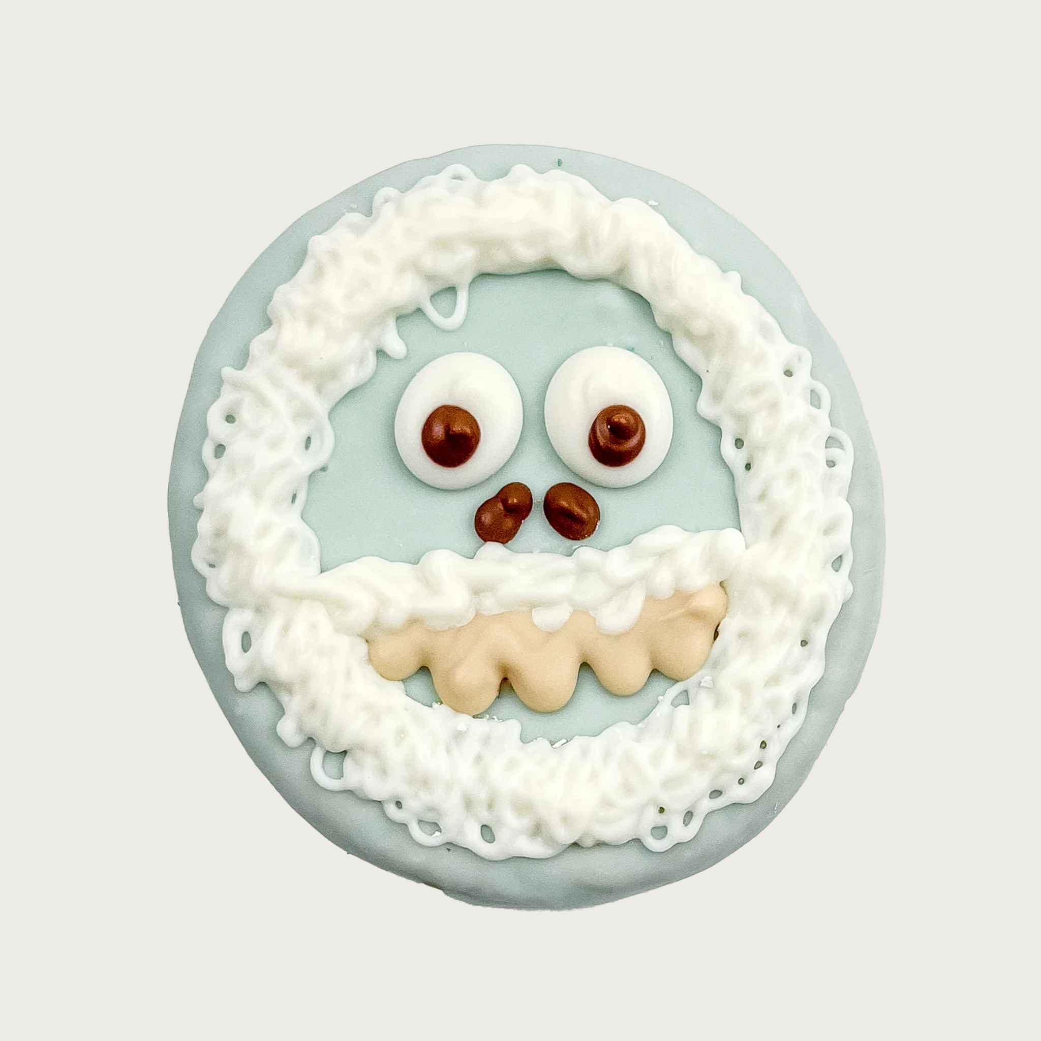 Dog cookie decorated to look like a yeti, or abominable snowman. It's covered in pale blue icing, with white icing in thick drizzles to look like fur around its face and mouth. It has large, googly eyes, small nostrils, and cream-colored teeth.