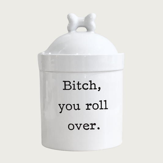 White ceramic dog treat jar with bone-topped lid. Sarcastic text in center reads "Bitch, you roll over." in black.