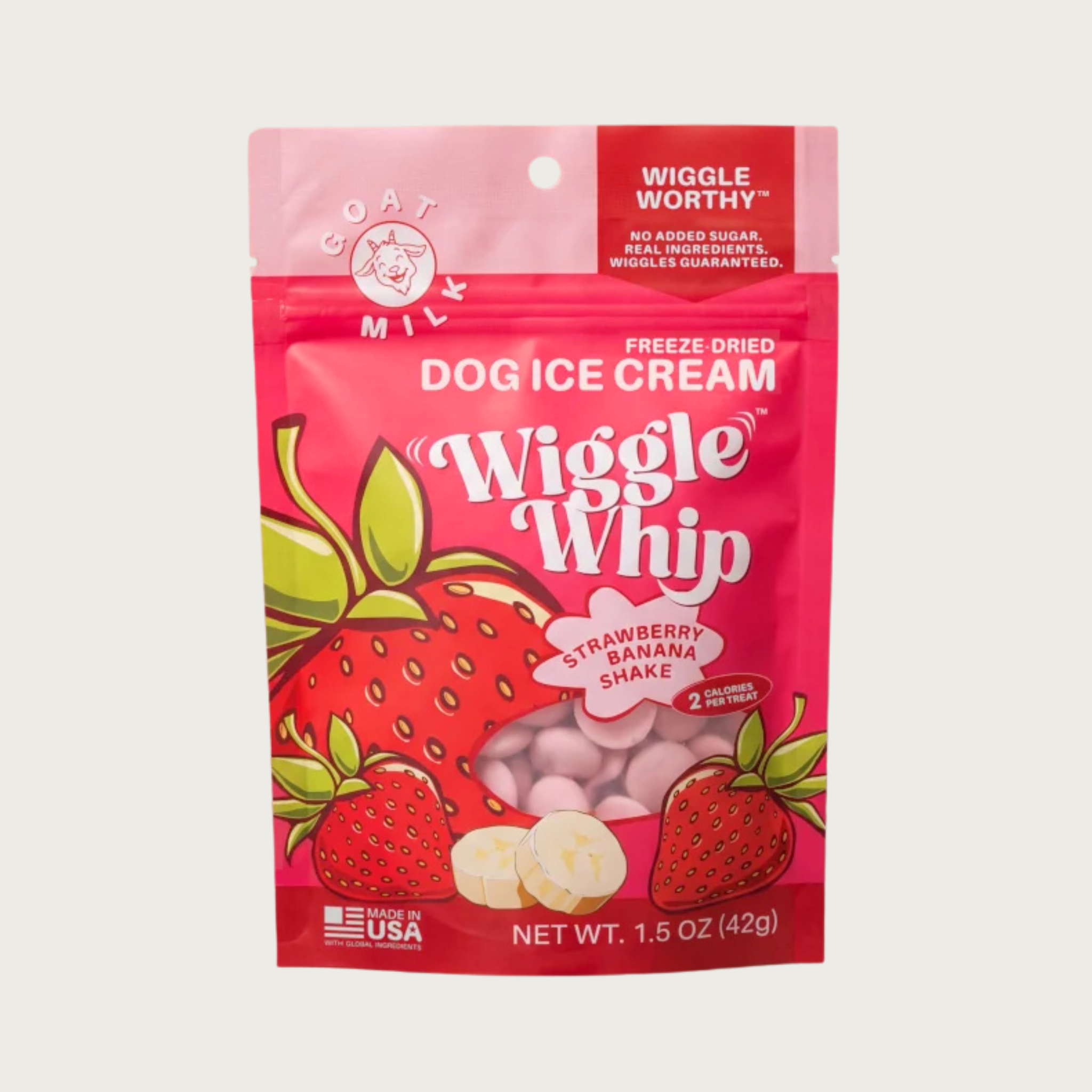 A pouch of Wiggle Whip Freeze Dried Dog Ice Cream in Strawberry Banana Shake flavor. The packaging is bright red with illustrations of whole strawberries and sliced banana, with a small transparent window showing the small, pink, disc shaped treats.