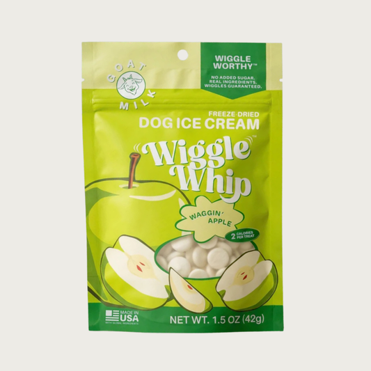 A pouch of Wiggle Whip Freeze Dried Dog Ice Cream in Waggin' Apple flavor. The packaging is bright green with illustrations of a whole and sliced apple, with a small transparent window showing the small, white, disc shaped treats.