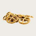 Load image into Gallery viewer, Closeup of a small pile of Peanut Butter Pretzels dog treats. They are thin and light brown in color, with a grainy texture.
