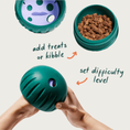 Load image into Gallery viewer, The Walkabout toy opened up to show the adjustable dial, and one half full of Puzzle Treats. Text pointing to both halves reads: "add treats or kibble" and "set difficulty level".
