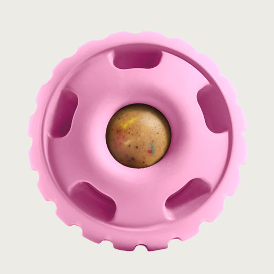 Medium shade of pink, round Pupsicle toy. Center has a small, depressed, round open area for dog to access a treat. Around this opening, are 5 smaller slot-type openings (called "drool slots"), to provide additional access and collect excessive drool. Bottom half of toy is solid rubber with an indentation to twist toy apart.