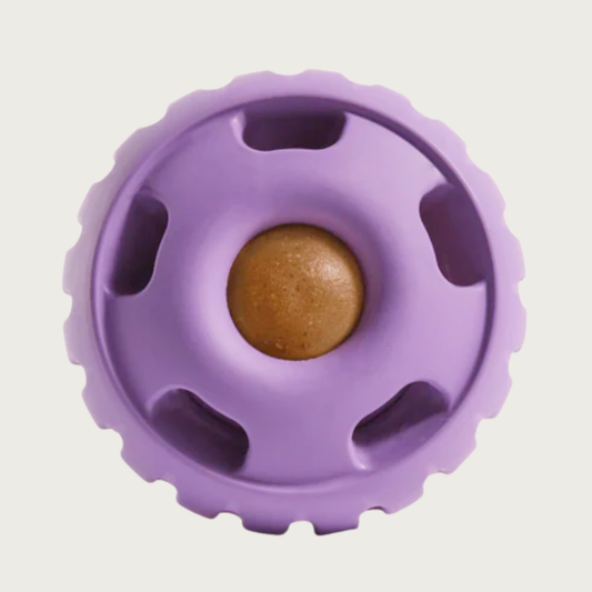 Lavender colored, round Pupsicle toy. Center has a small, depressed, round open area for dog to access a treat. Around this opening, are 5 smaller slot-type openings (called "drool slots"), to provide additional access and collect excessive drool. Bottom half of toy is solid rubber with an indentation to twist toy apart.