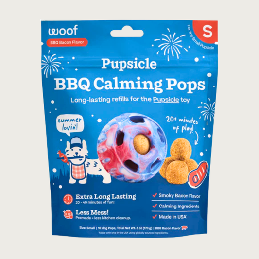 10 ct bag of small Woof BBQ Calming Pops, long-lasting refill treats for the Pupsicle toy to promote calm. Extra long lasting, less mess. Image of red, white & blue tie-dyed Pupsicle toy is in center, with refill pop inside, with sample pops clustered to the right. They are round, tan colored balls, coated with bacon powder.