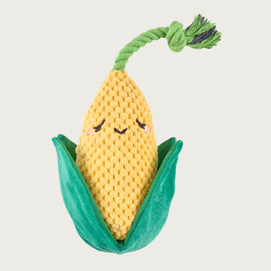 Plush dog toy shaped like an ear of corn. Its body is a nubby yellow plush with dark green husks, and green rope coming out the top of the corn.