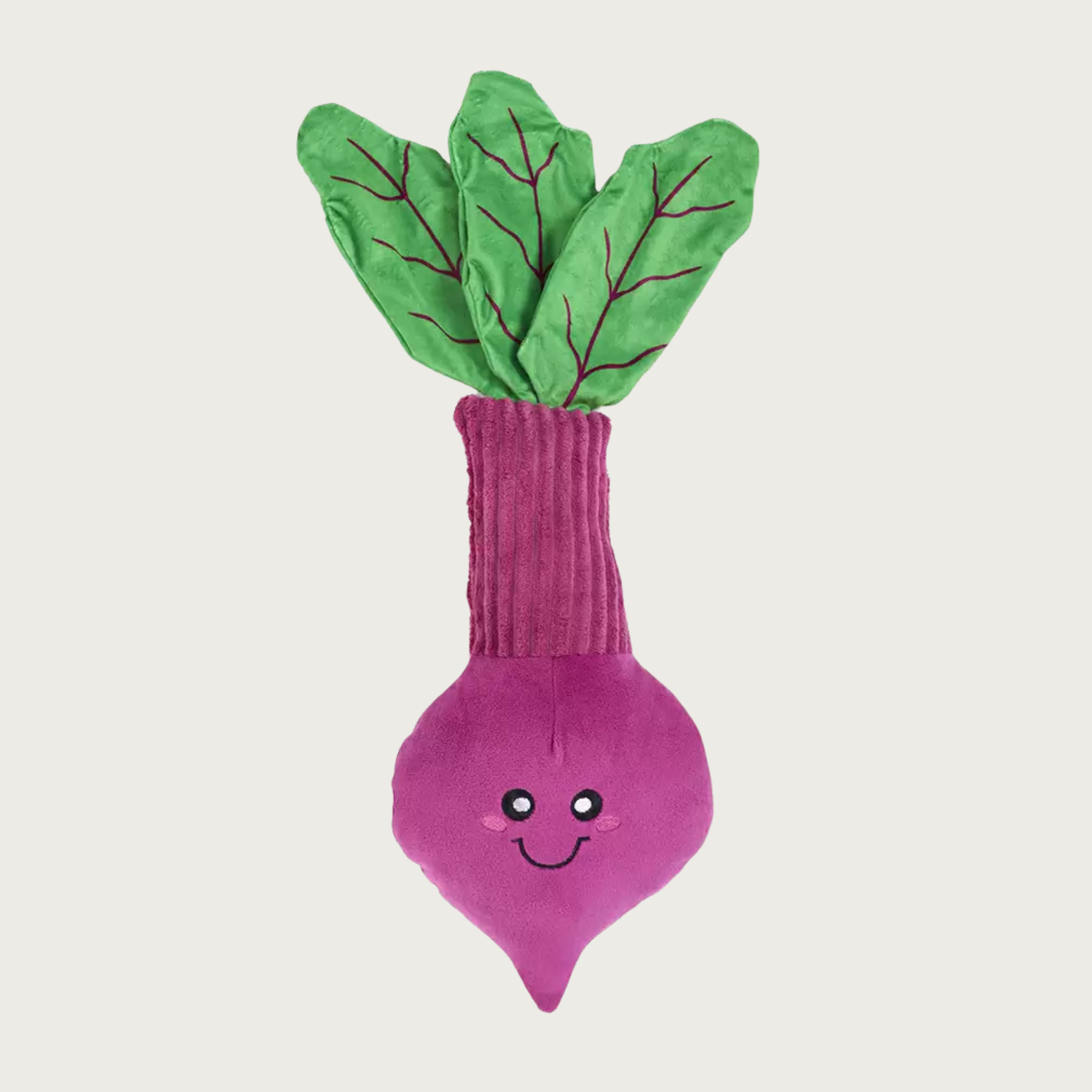 Plush dog toy shaped like a beet with green leafy top, a ribbed magenta stem, and a smiling purple root with embroidered eyes and mouth.