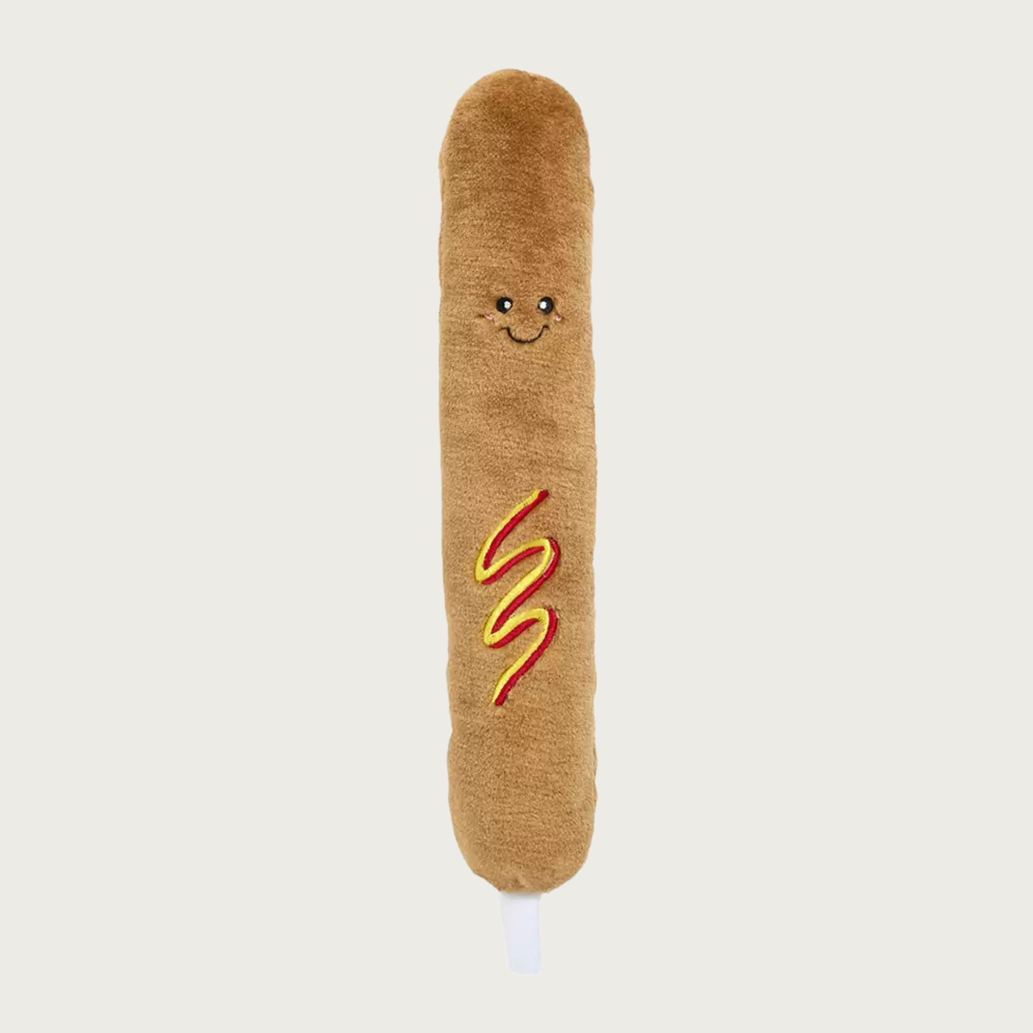 A plush corn dog shaped dog toy with a brown fuzzy body, embroidered smiling face, and red and yellow wavy mustard & ketchup details in the center of its body.