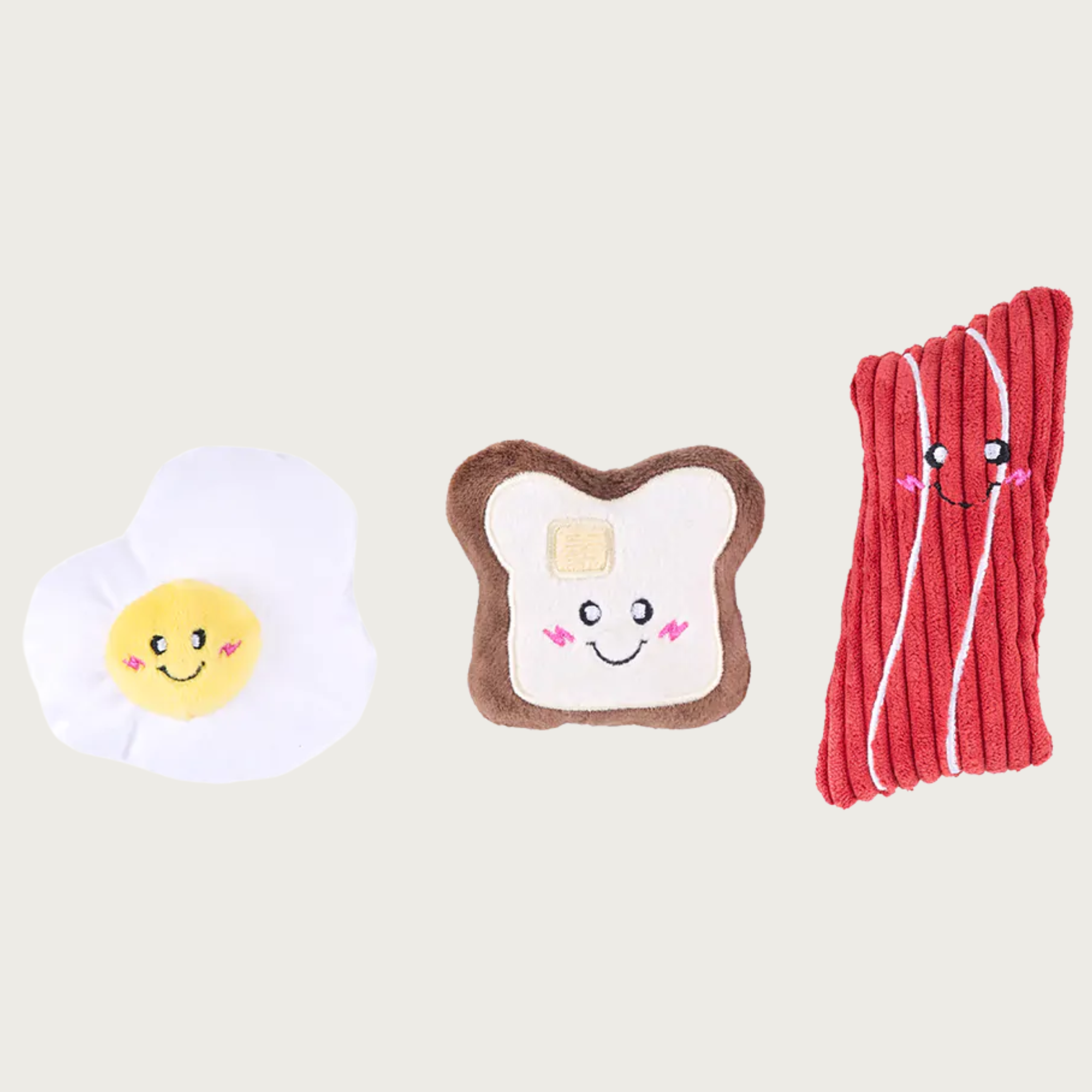 Three small, plush dog toys shaped like a fried egg, toast with pat of butter, and red slice of bacon.