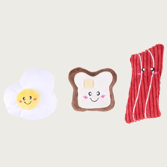 Three small, plush dog toys shaped like a fried egg, toast with pat of butter, and red slice of bacon.