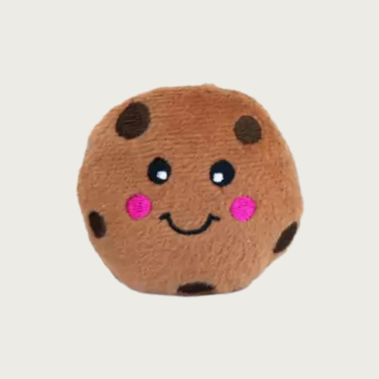 Plush dog toy shaped like a chocolate chip cookie. It has a a brown fuzzy body with dark brown chocolate spots, embroidered black eyes and smile, and pink cheeks.