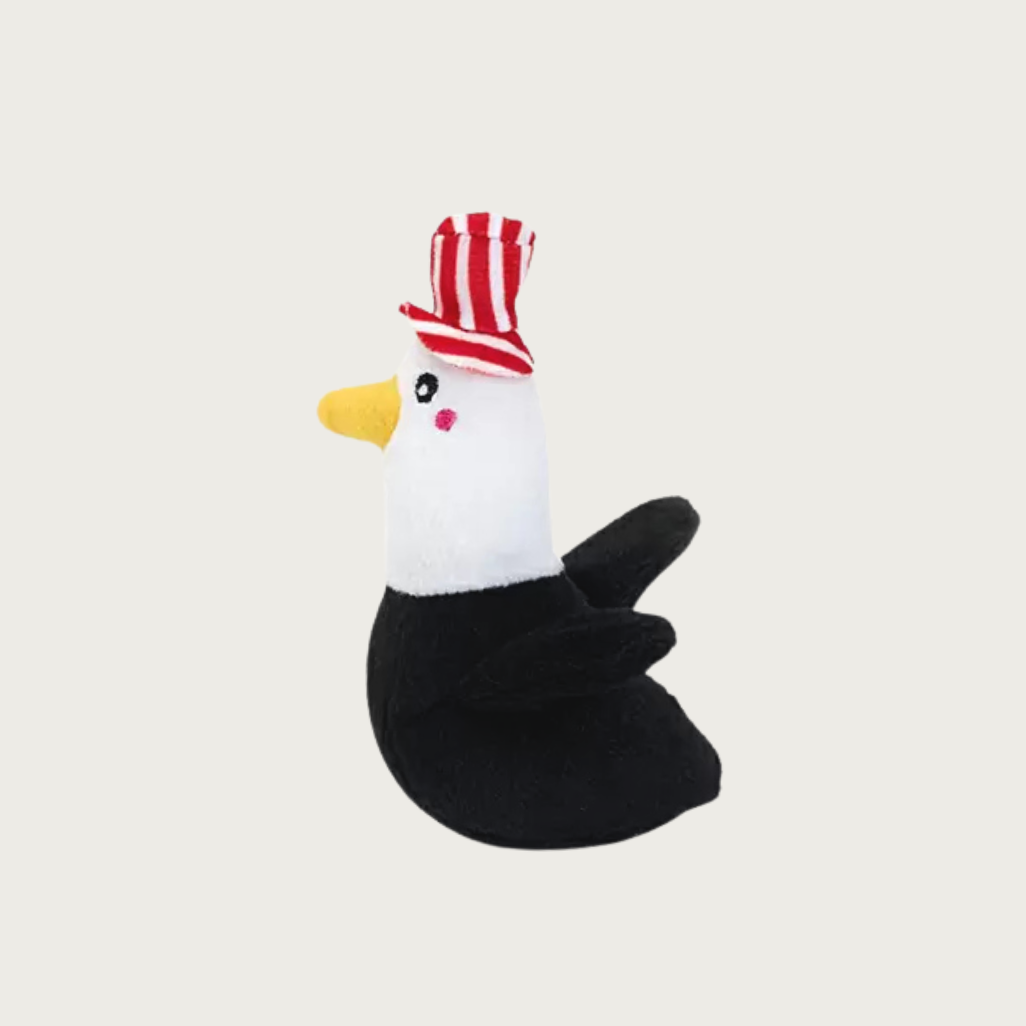 A small, plush bald eagle dog toy wearing a red & white striped top hat.